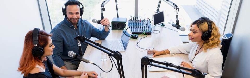 three persons sitting at a table with microphones